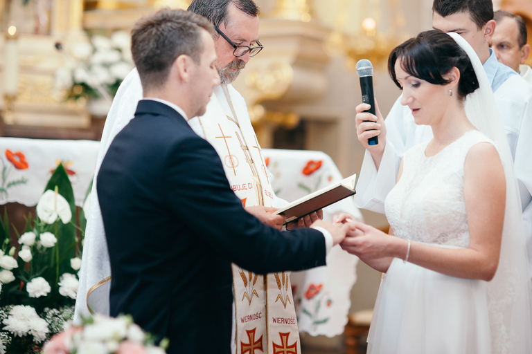 Pani młoda nakłada obrączkę Panu młodemu podczas ceremonii ślubnej w kościele - ślubna sesja zdjęciowa Ariany i Bartka