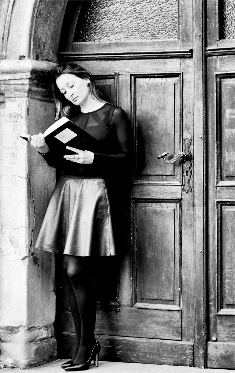 Portretowa sesja zdjęciowa w czerni i bieli. Mira stoi i czyta książkę przed bramą na krakowskim Kazimierzu.