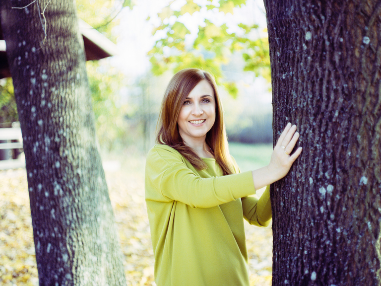 Portretowa sesja zdjęciowa Moniki w ciepłe, słoneczne, październikowe popołudnie. Monika opiera się o drzewo.