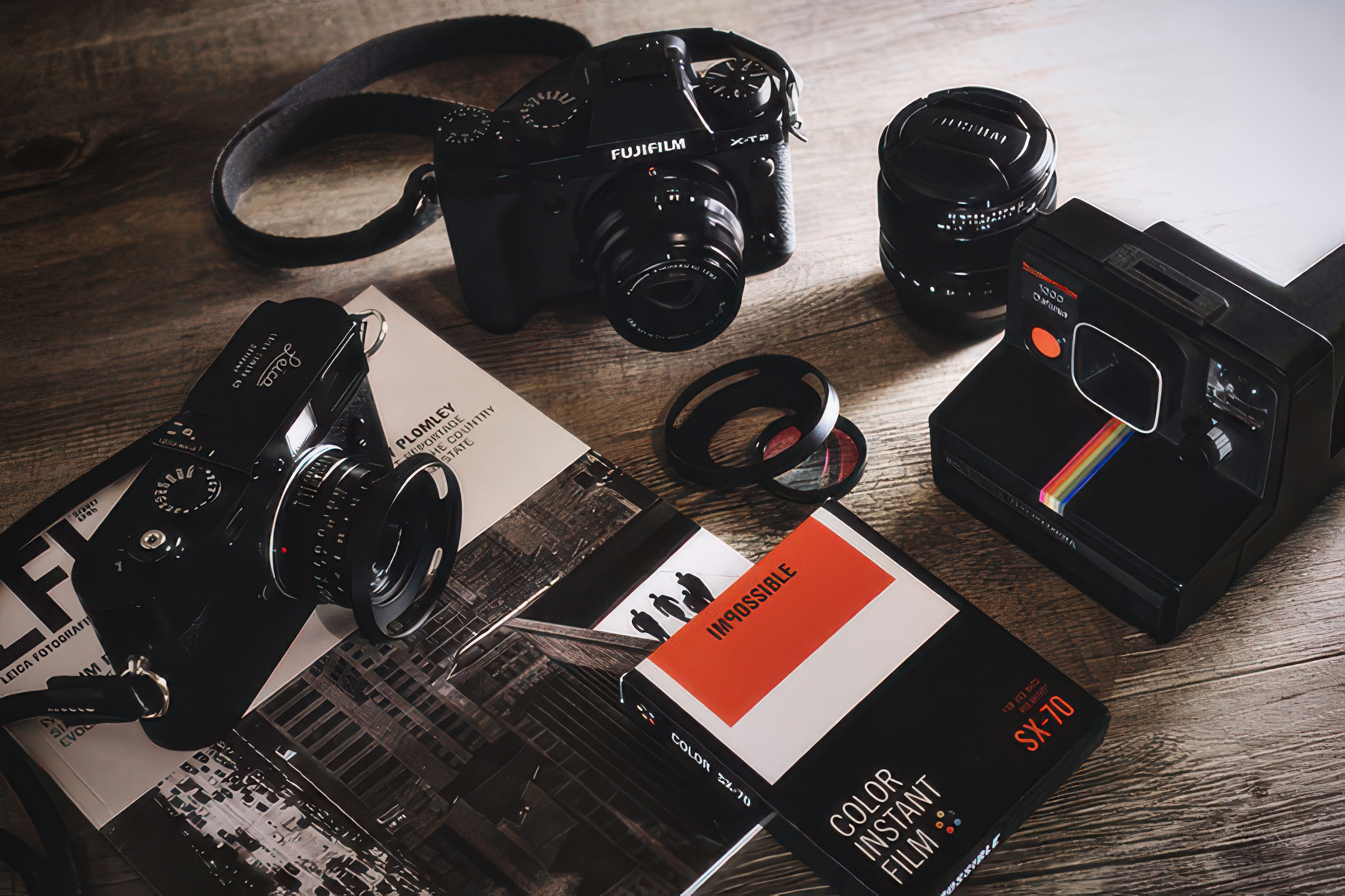 Aparaty Fujifilm i analogowy Polaroid SX-70 na stole – różne narzędzia fotografa i ich znaczenie w twórczości